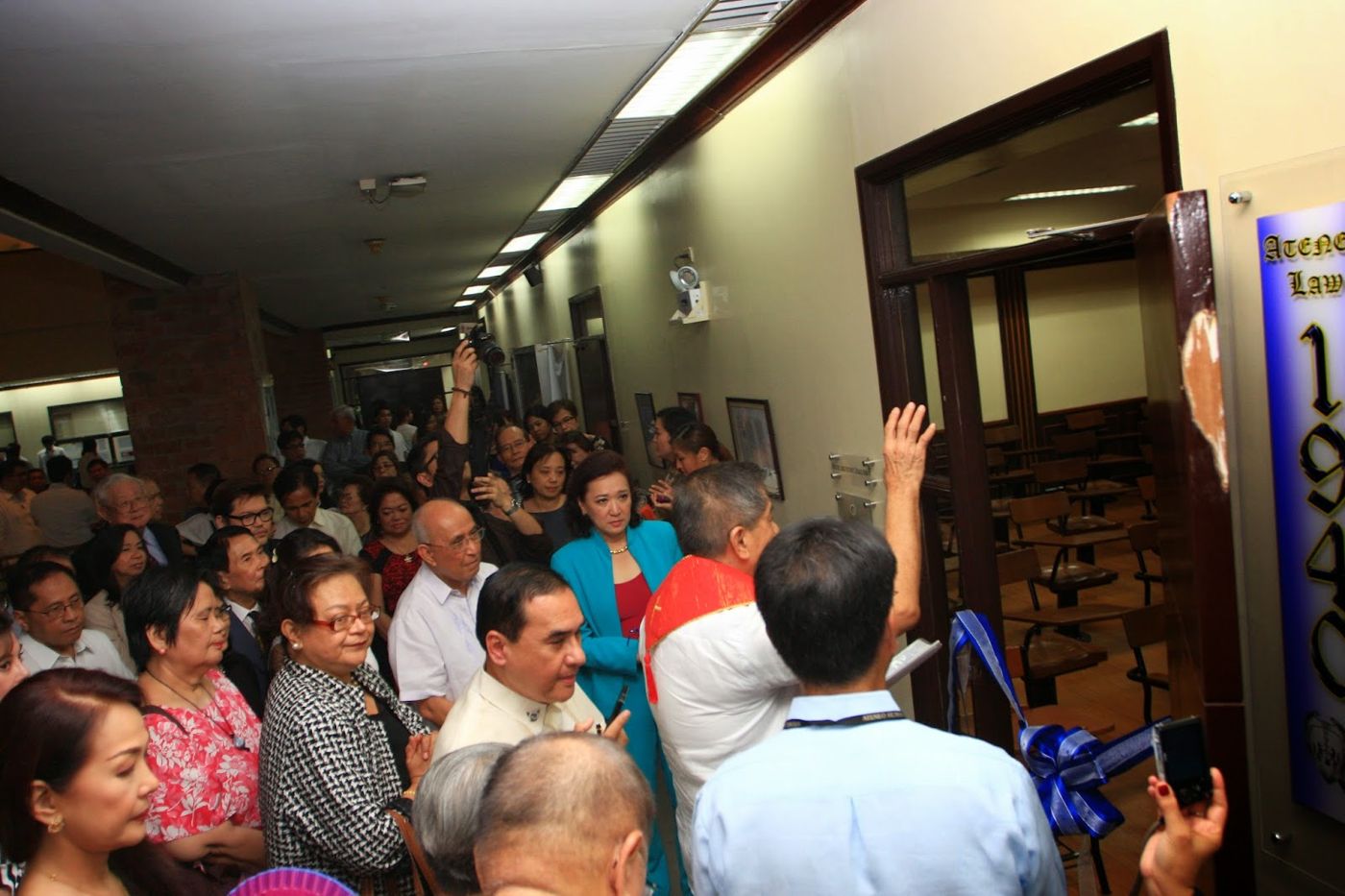 A priest blesses the door of the Rosales Room before a crowd